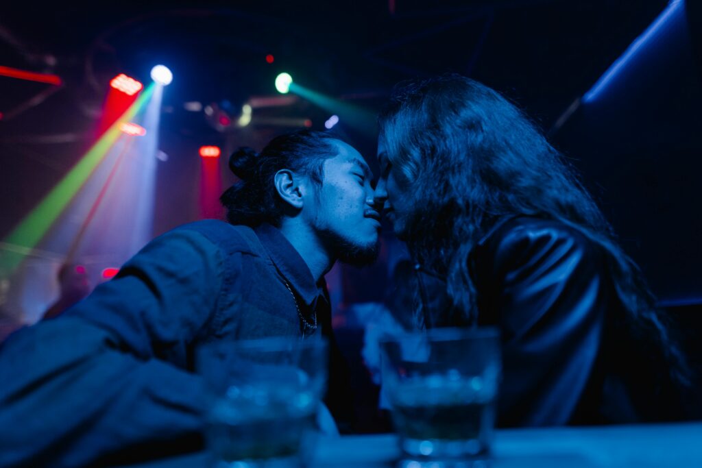 a couple kissing at a dark bar while strobe lights flash in the background