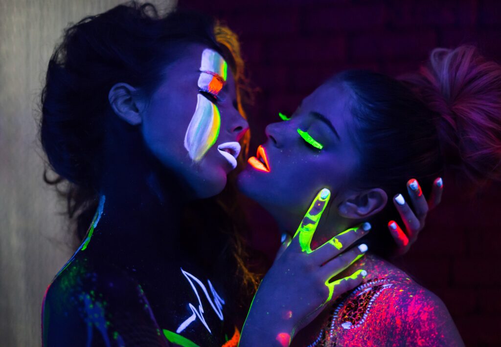 sexy women in uv neon paint in an embrace, close to kissing.